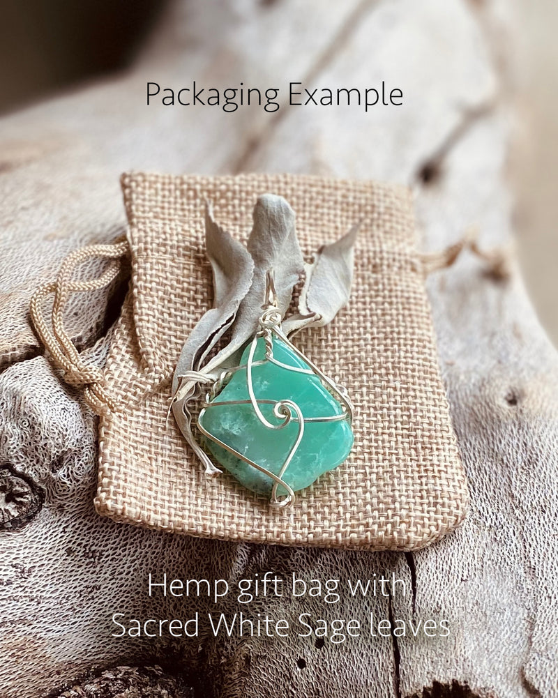 An example of our packaging showing a crysophrase crystal pendant on a natural toned hemp gift bag with some sage leaves.