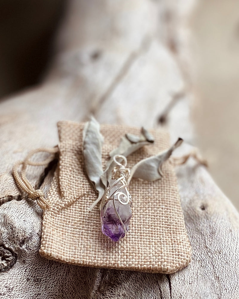 An example of our packaging showing a crysophrase crystal pendant on a natural toned hemp gift bag with some sage leaves.